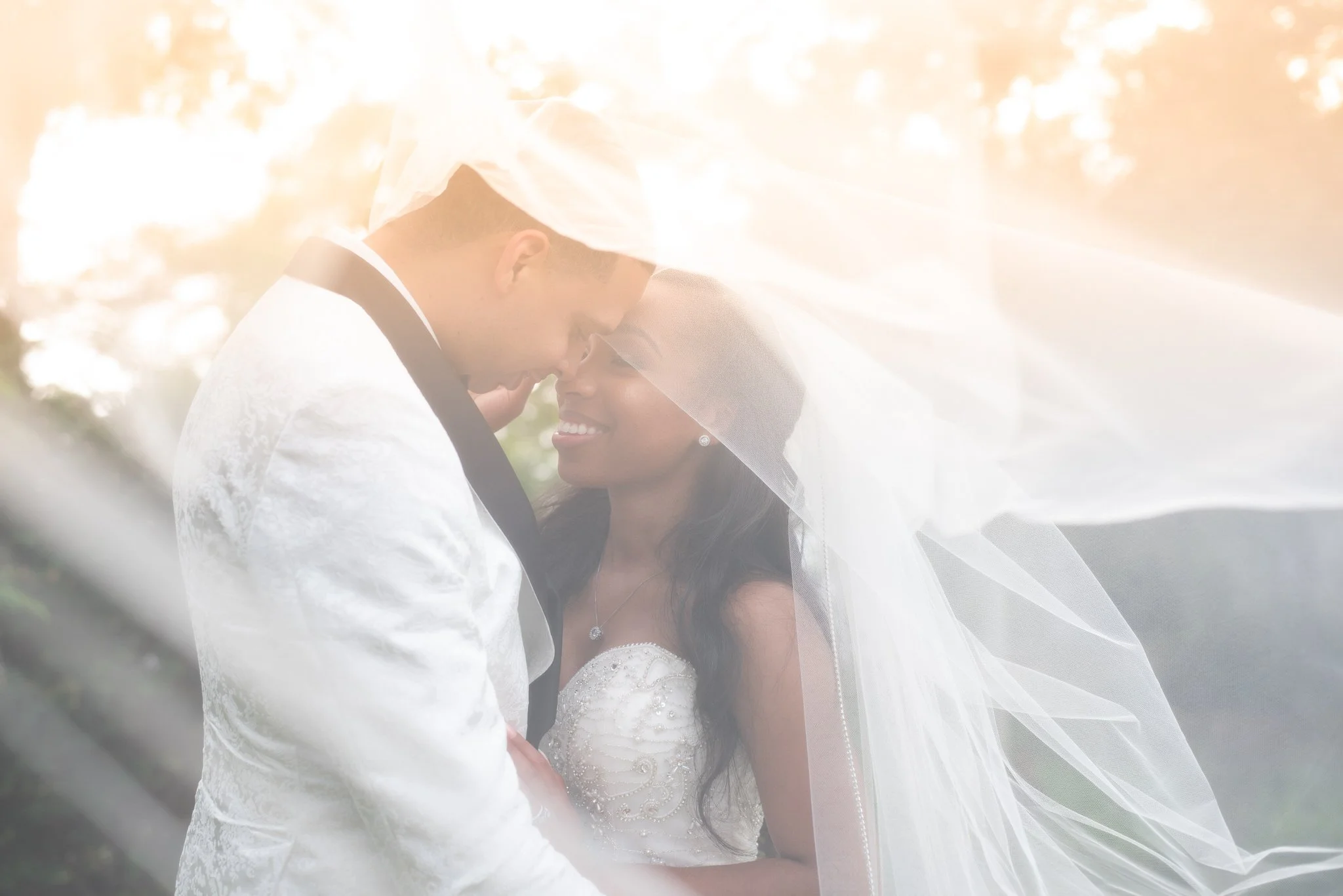 A bride and groom share an intimate moment under a wedding veil during sunset.