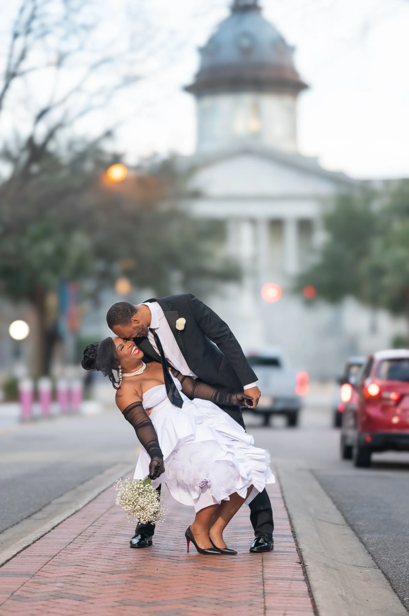 Couple dancing on a city sidewalk during their wedding, with a historic building in the background.